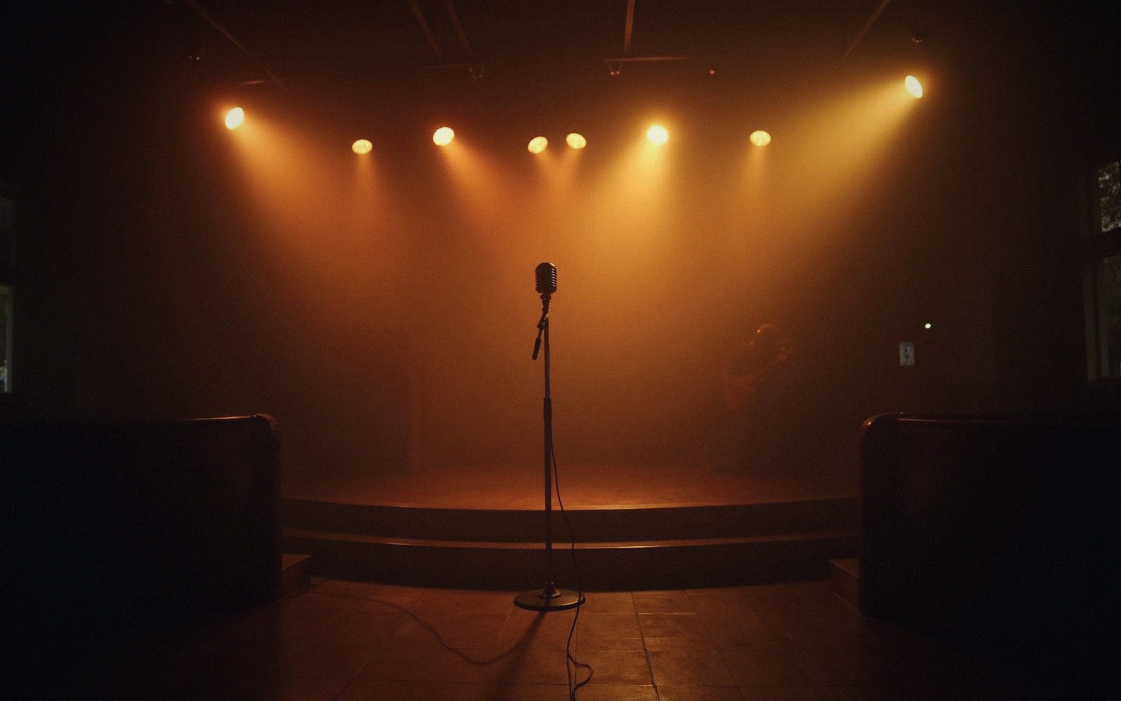 A vintage microphone stands alone on an empty stage under warm spotlights